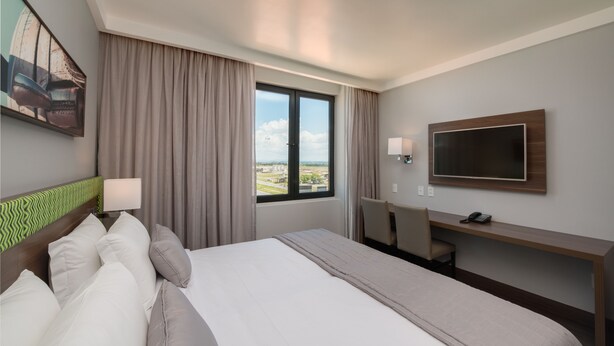 A hotel room with a bed, a desk, a TV, and a window with a view of the city. - Linx Confins by Wish (Confins)