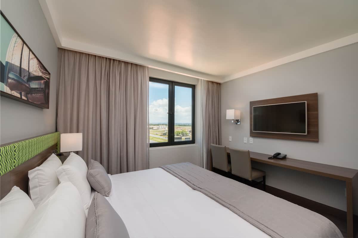 Habitación de hotel con cama, escritorio, televisor y ventana con vistas a la ciudad.