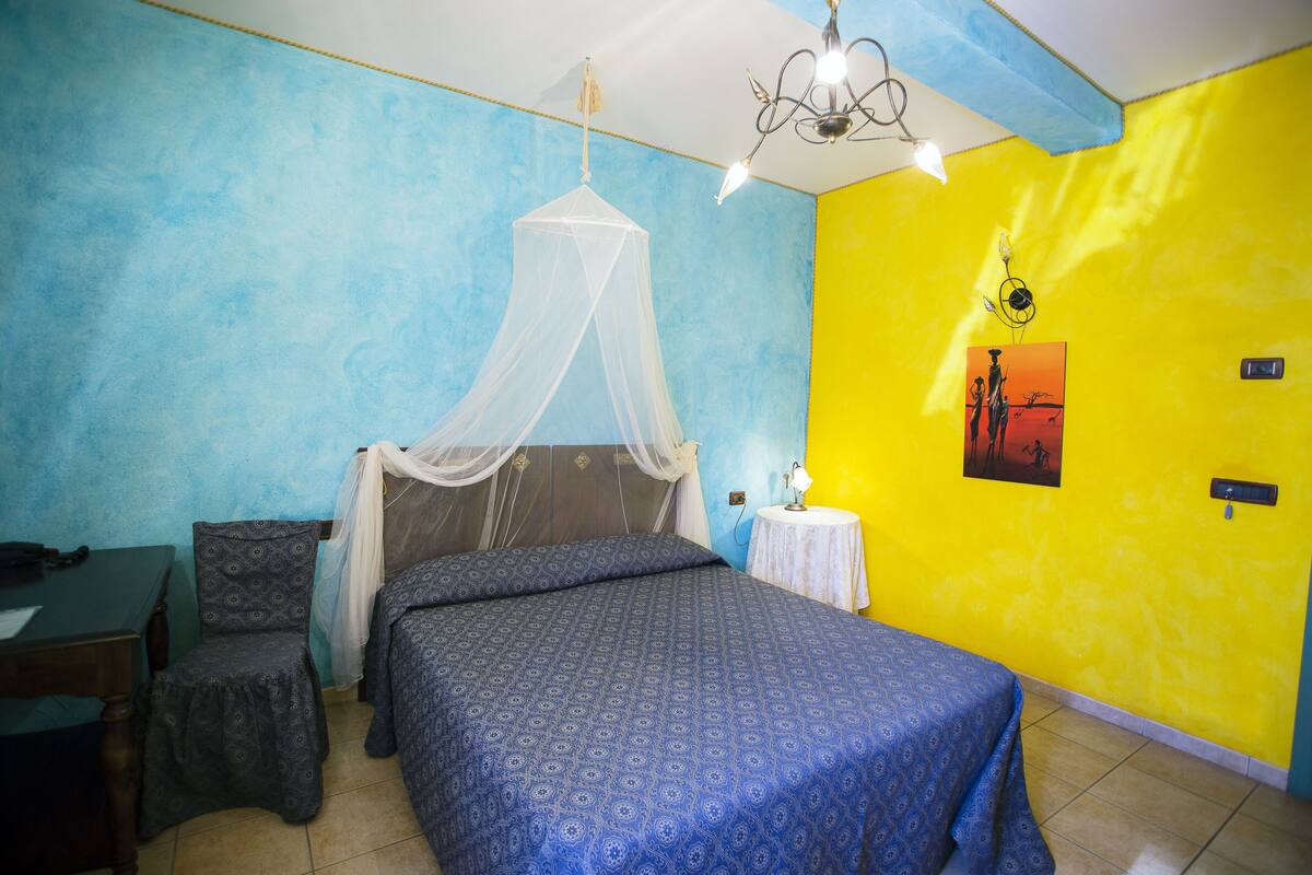 Una habitación con una cama, una silla, una mesa y una pared con una decoración azul y amarilla.