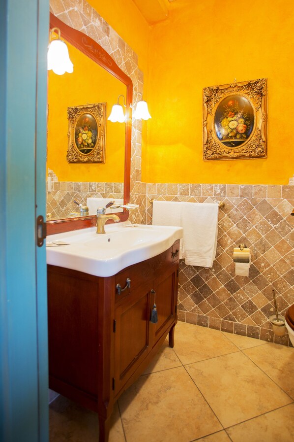 A bathroom with a white sink, wooden vanity, two framed floral paintings, and a tiled backsplash. - Casale Villa Giulia (Lesina)