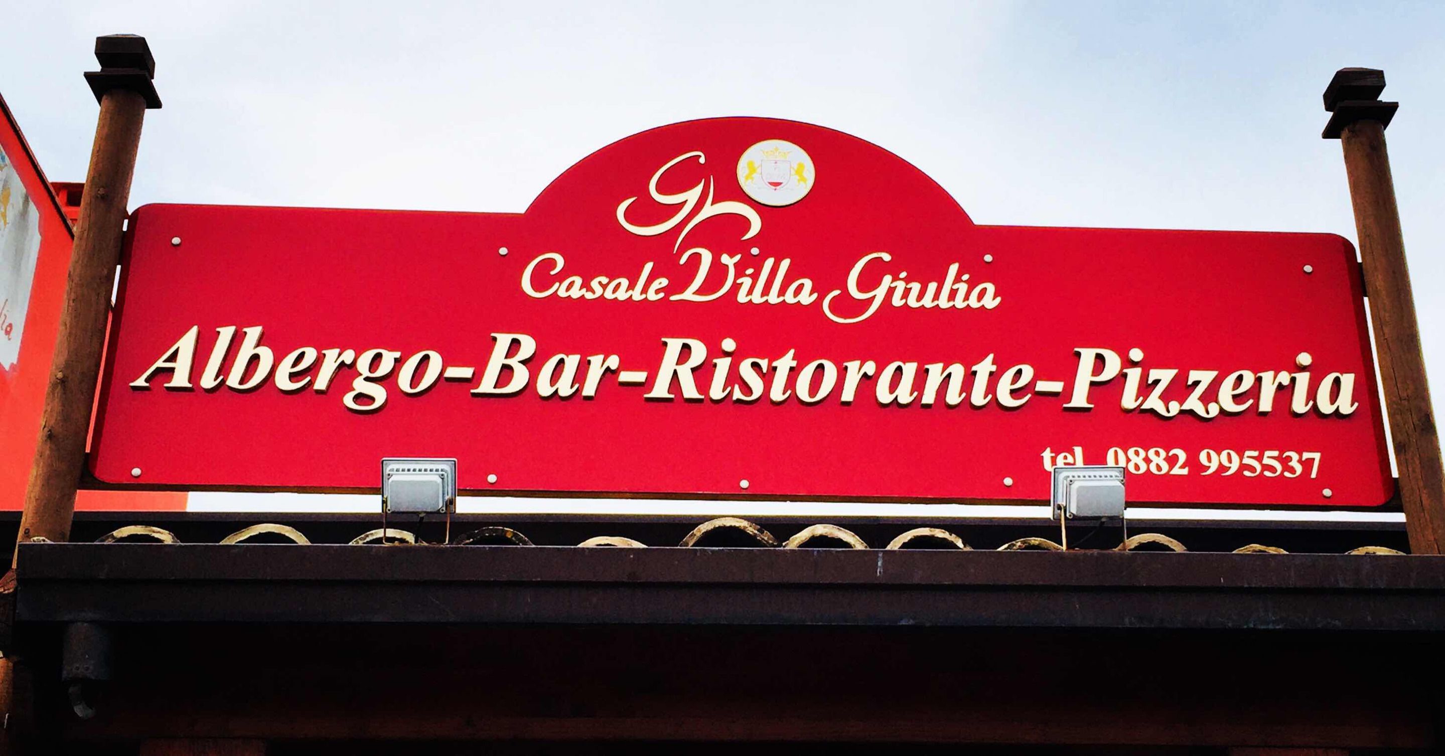A red sign for Albergo-Bar-Ristorante-Pizzeria with the name Casale Villa Giulia and a phone number.