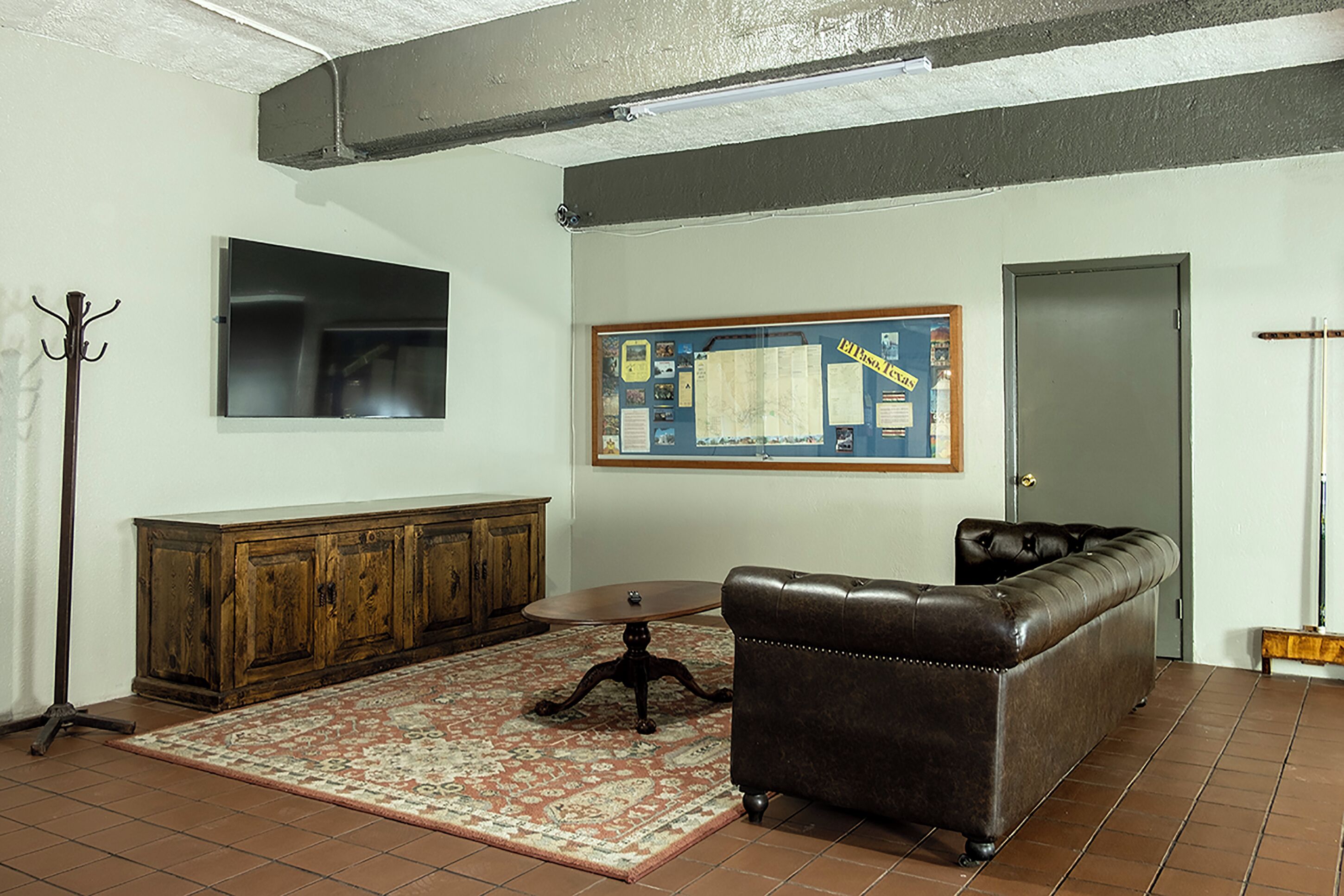 A living room with a brown leather sofa, a wooden cabinet, a small round table, and a patterned rug.