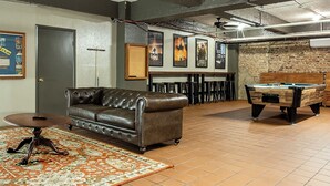 A lounge area with a leather sofa, a pool table, and a bar area with stools. - The Gardner  (El Paso)