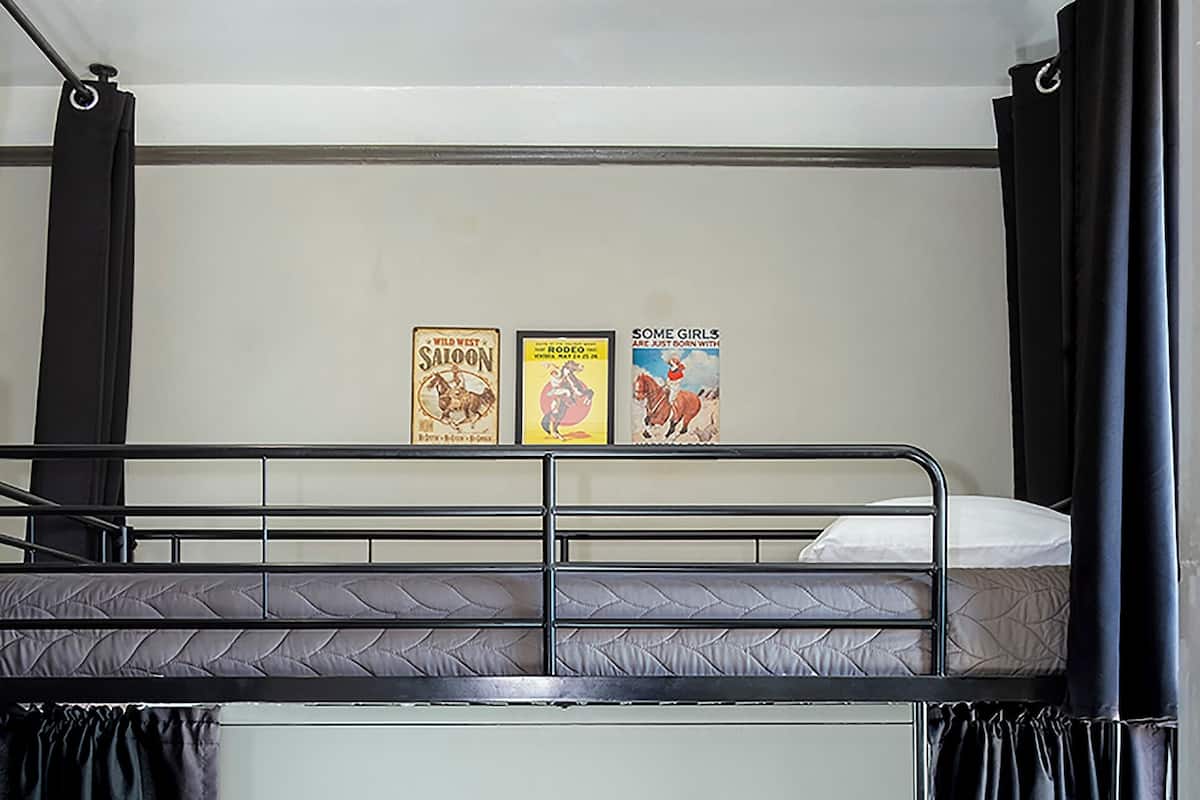 Habitación con literas, dos carteles en la pared, cortinas negras y alfombra gris.