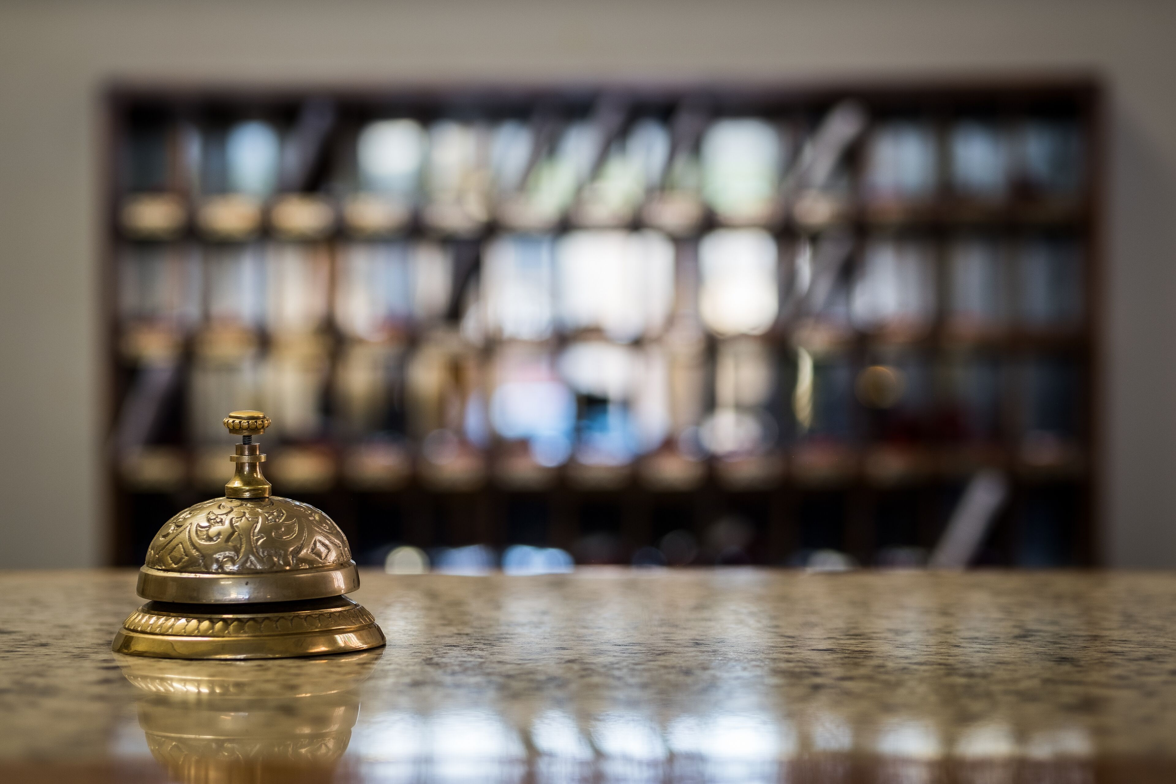 A brass bell on a polished marble surface with a blurred background of shelves and bottles.