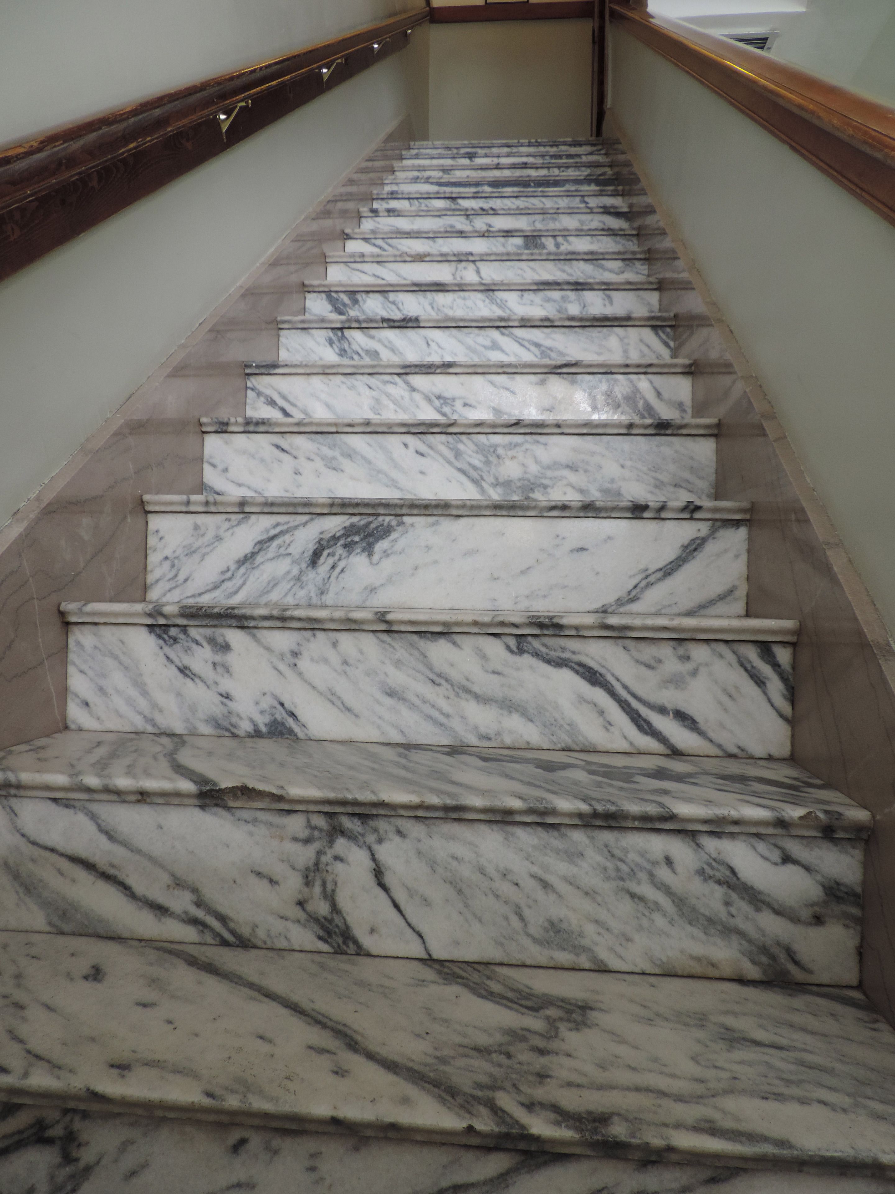 A marble staircase with a wooden handrail and beige walls.