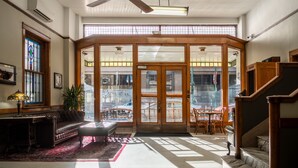 A spacious lobby with a large wooden staircase, a leather sofa, and a dining area with a view of the street. - The Gardner  (El Paso)