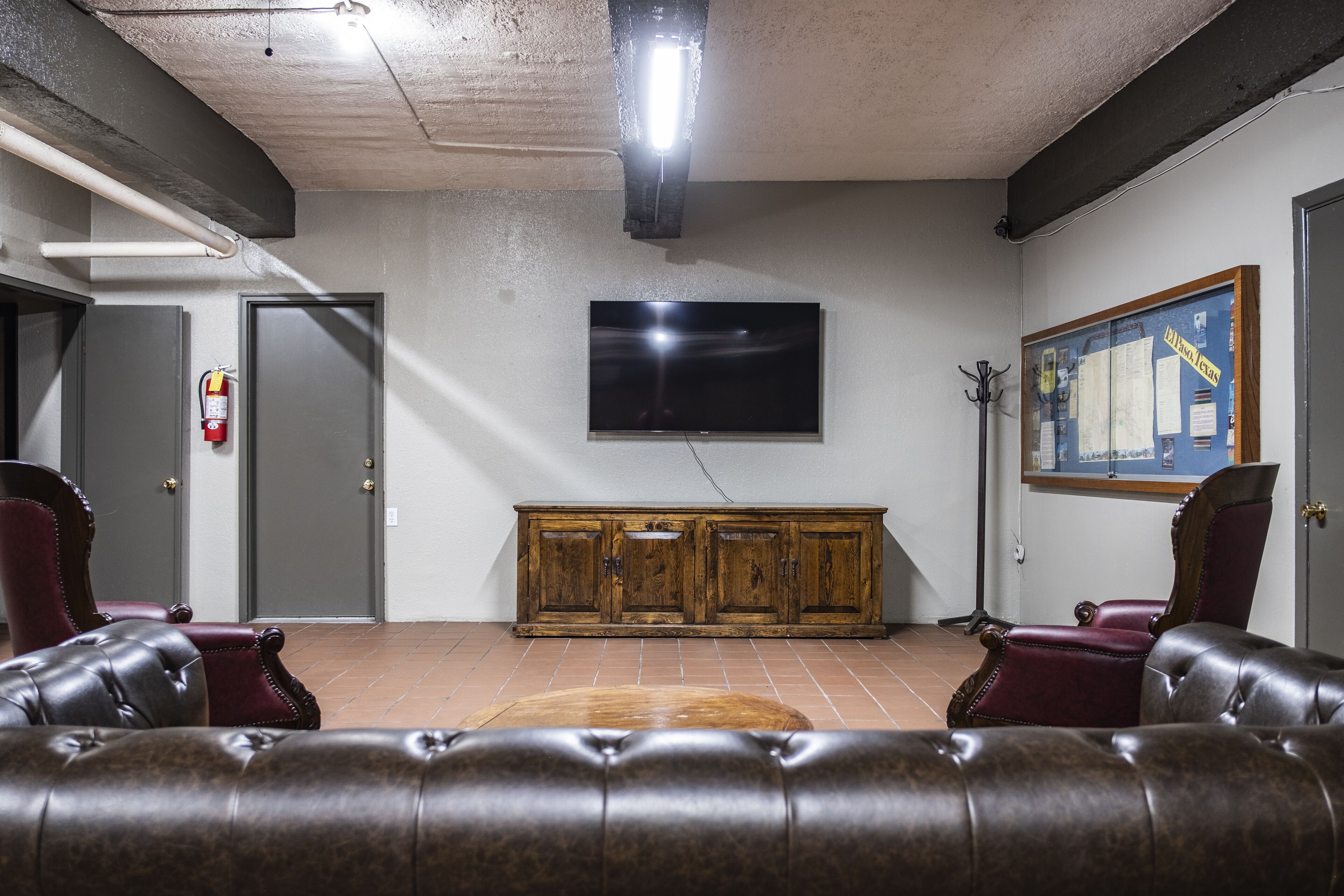 Una habitación con un sofá de cuero, un armario de madera, un televisor de pantalla plana y un extintor.