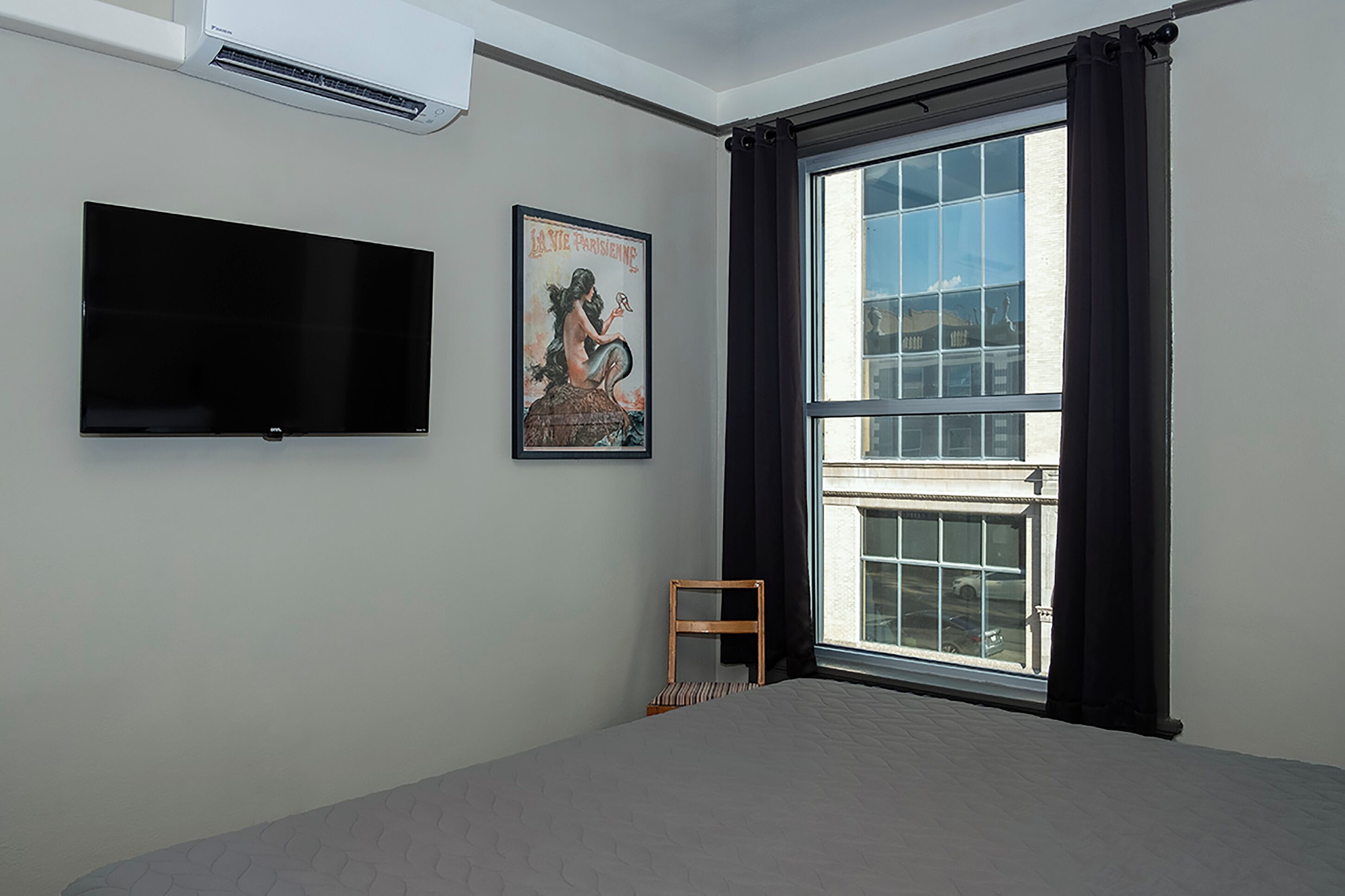 A bedroom with a large window, a flat-screen TV, and a poster on the wall.