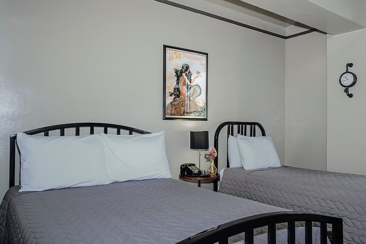 Habitación de hotel con dos camas, un reloj en la pared y un cartel con una mujer a caballo.