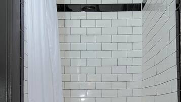 Une douche aux murs recouverts de carreaux blancs et au sol orné d’un motif noir et blanc.