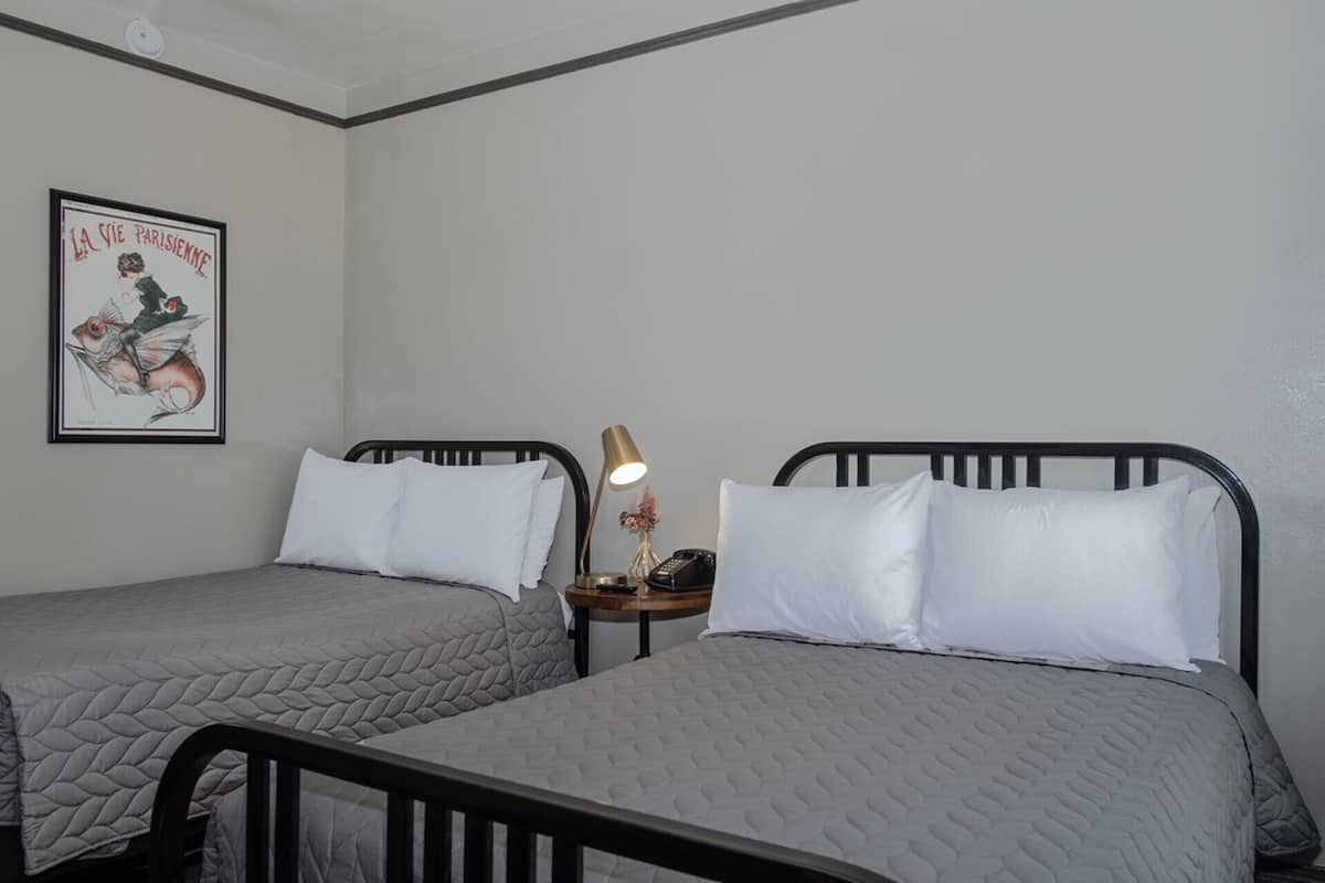Dos camas individuales con ropa blanca, una mesita de noche con lámpara, teléfono y un cuadro en la pared.
