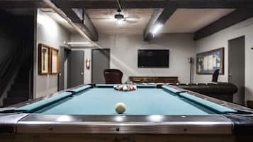 A pool table with balls, a ceiling fan, a TV on the wall, and a staircase.