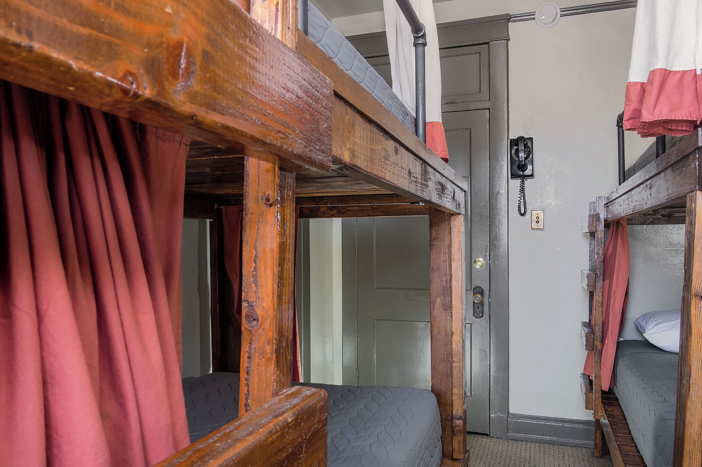 Une chambre avec un lit superposé, une tête de lit en bois, un téléphone et une porte.