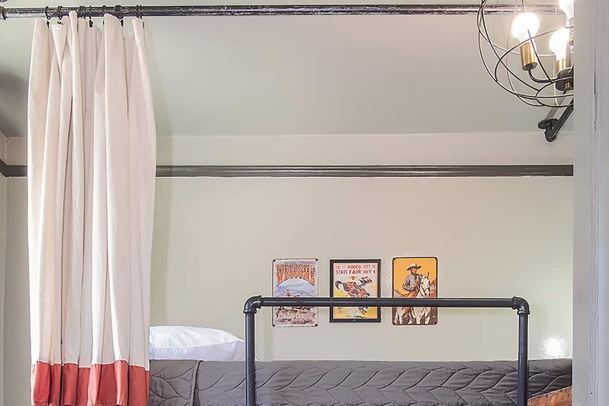 Una litera con escalera de madera, una cortina y un aplique de pared.