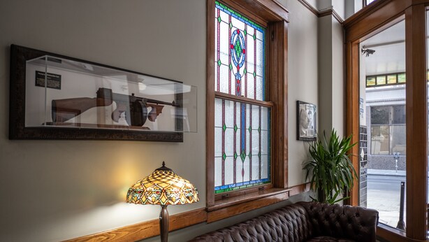 A lobby with a leather sofa, a stained glass window, and a lamp. - The Gardner  (El Paso)