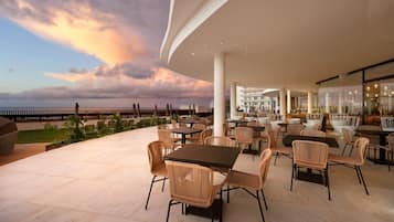 Un patio al aire libre con mesas y sillas, con vista a la playa.