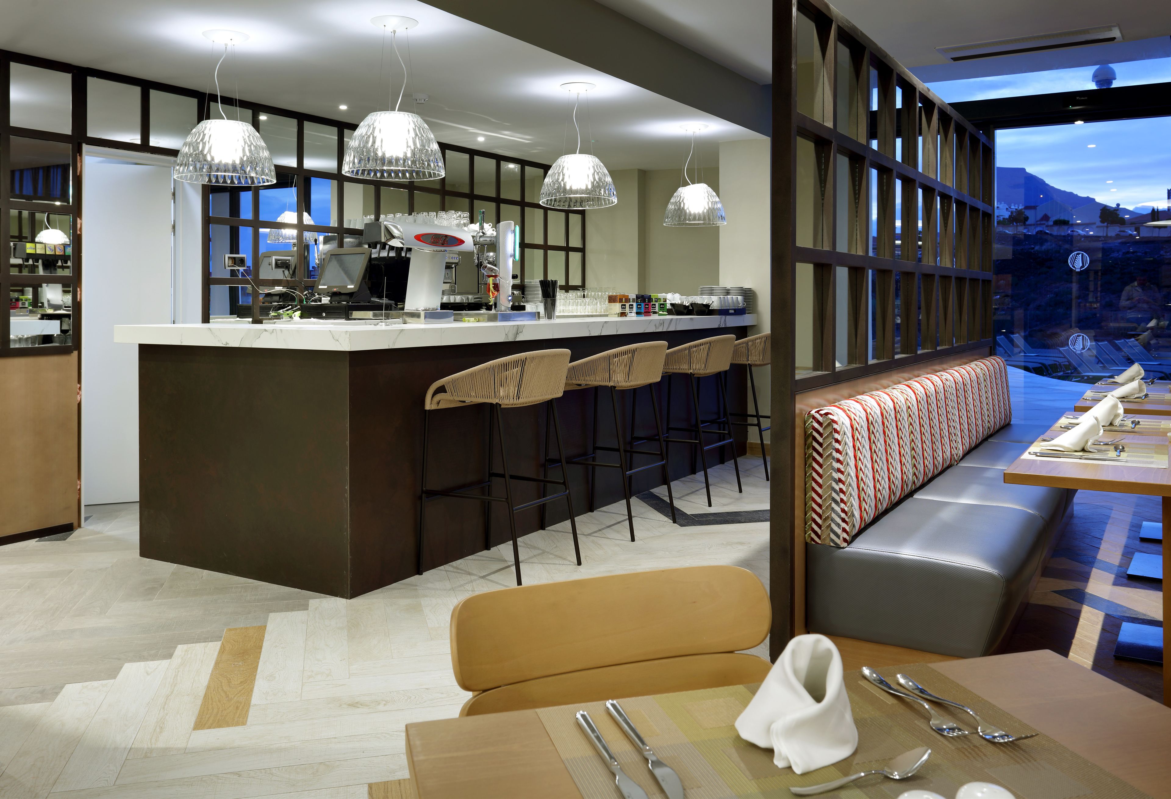 A modern kitchen with a central island, bar stools, and a seating area with a bench and table.