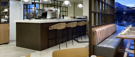 A modern kitchen with a central island, bar stools, and a seating area with a bench and table.