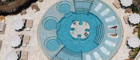 Una piscina circular con varias zonas de estar y sillones de descanso alrededor.