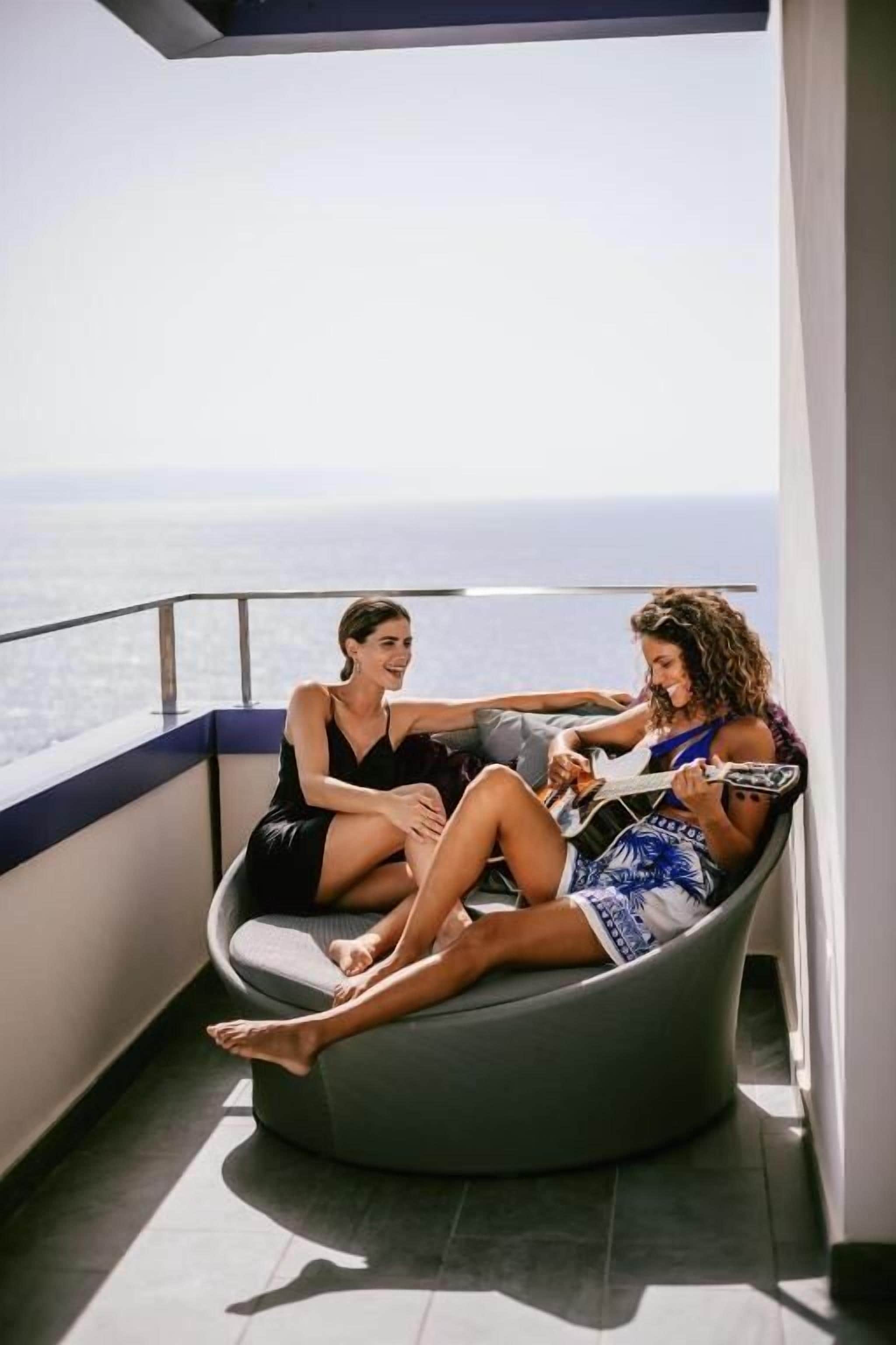 Duas pessoas sentadas num banco curvo numa varanda com vista para a cidade.