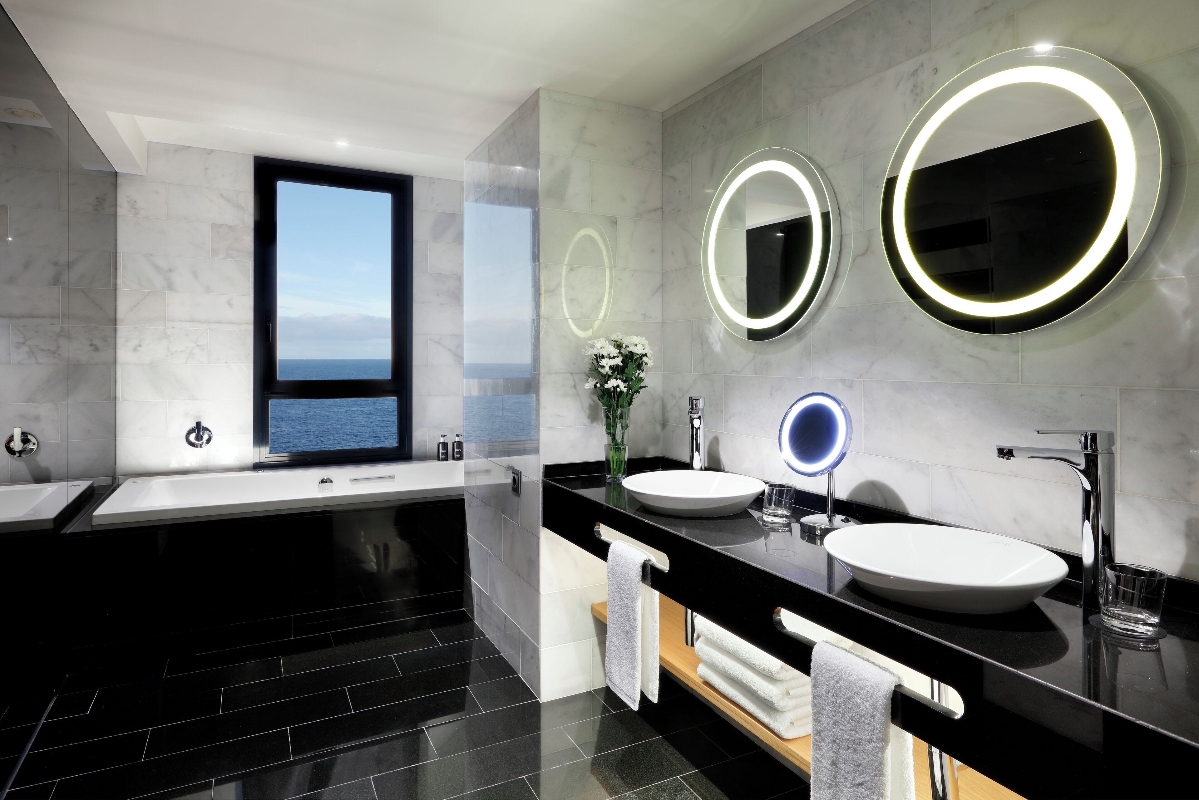 A modern bathroom with two sinks, a large mirror, and a bathtub.