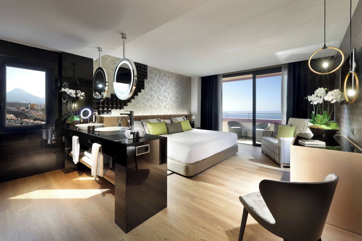 A modern hotel room with a bed, desk, and bathroom, featuring a city view.