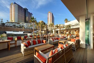 Un bar en la azotea con asientos al aire libre, palmeras y edificios altos al fondo.