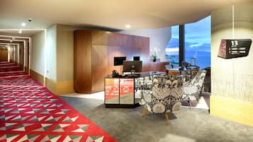 Un hall de hotel con mostrador de recepción, un sofá estampado, alfombra roja y un ventanal con vistas.