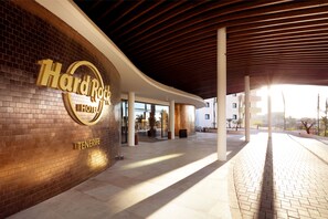 The exterior of the Hard Rock Hotel in Tenerife, featuring a brick facade, a curved roof, and a paved walkway.