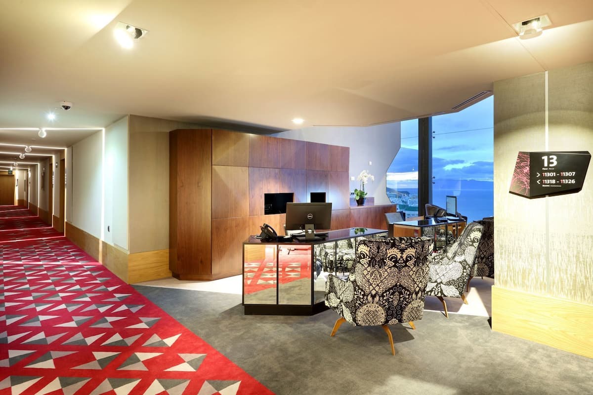 Hotellin aula, jossa on punainen matto, puinen vastaanottotiski ja suuri ikkuna, josta avautuu näkymä.