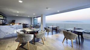 Un comedor moderno con vista al mar, que cuenta con encimeras de mármol, sillas contemporáneas y una zona de bar con televisor.