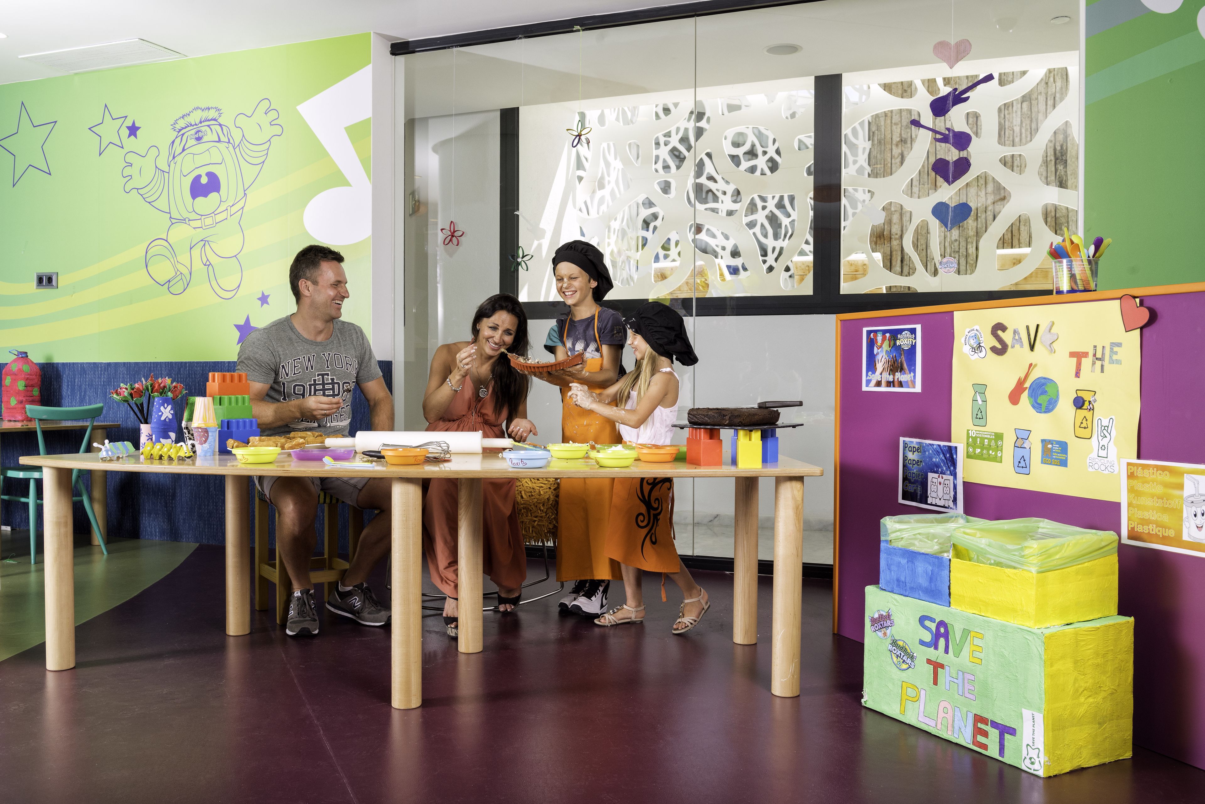 A group of people sitting at a table with food, in a room with educational posters and a 'Save the Planet' display.