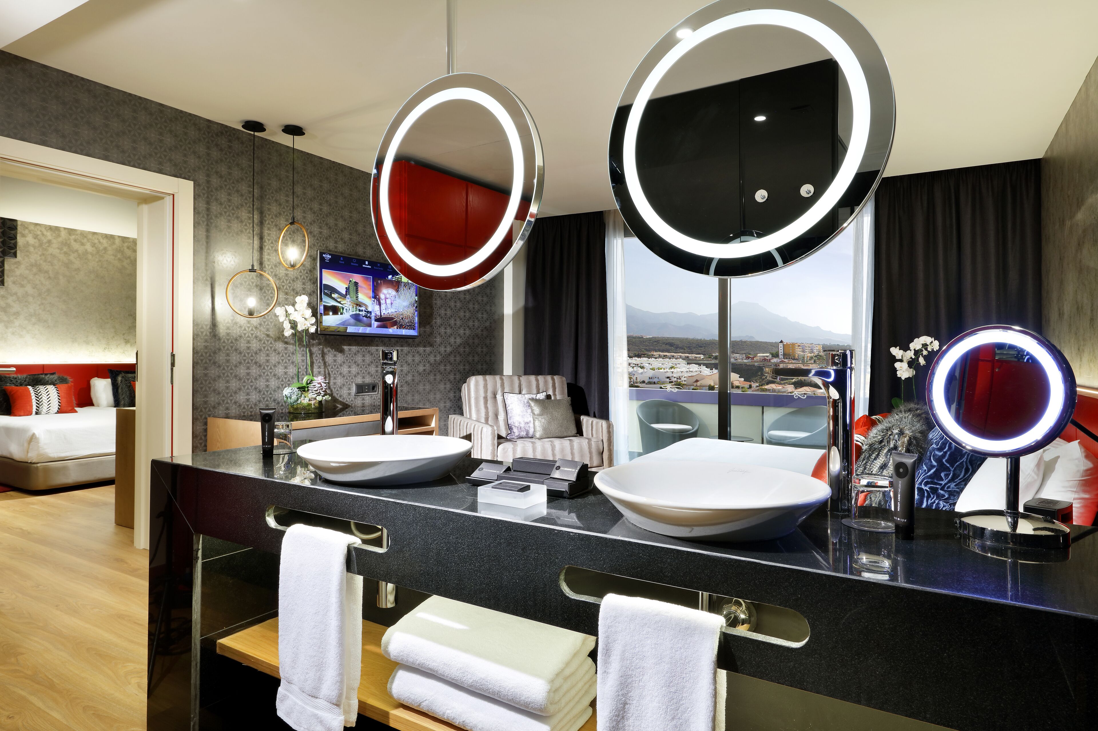 Un baño de hotel moderno con dos espejos grandes, un tocador con dos lavamanos, un sofá y un televisor.