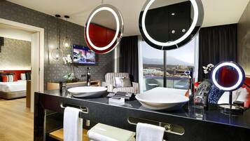 Un baño de hotel moderno con dos espejos grandes, un tocador con dos lavamanos, un sofá y un televisor.