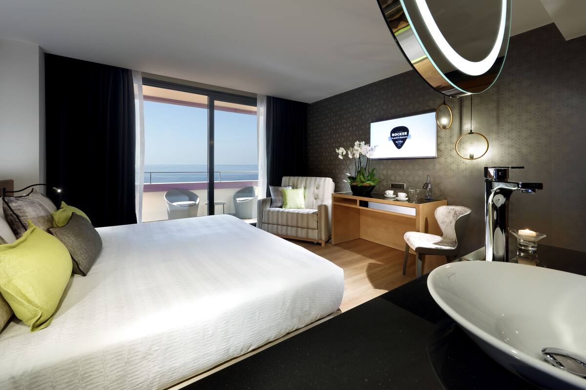 Moderni hotellihuone, jossa on suuri sänky, työpöytä, tuoli, kylpyammeella varustettu kylpyhuone ja näkymä merelle.