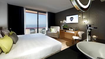 Una habitación de hotel moderna con una cama grande, un escritorio, una silla, un baño con bañera y vistas al océano.