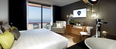 A modern hotel room with a large bed, a desk, a chair, a bathroom with a bathtub, and a view of the ocean.
