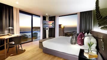 A modern hotel room with a large bed, a desk, a chair, and a TV.
