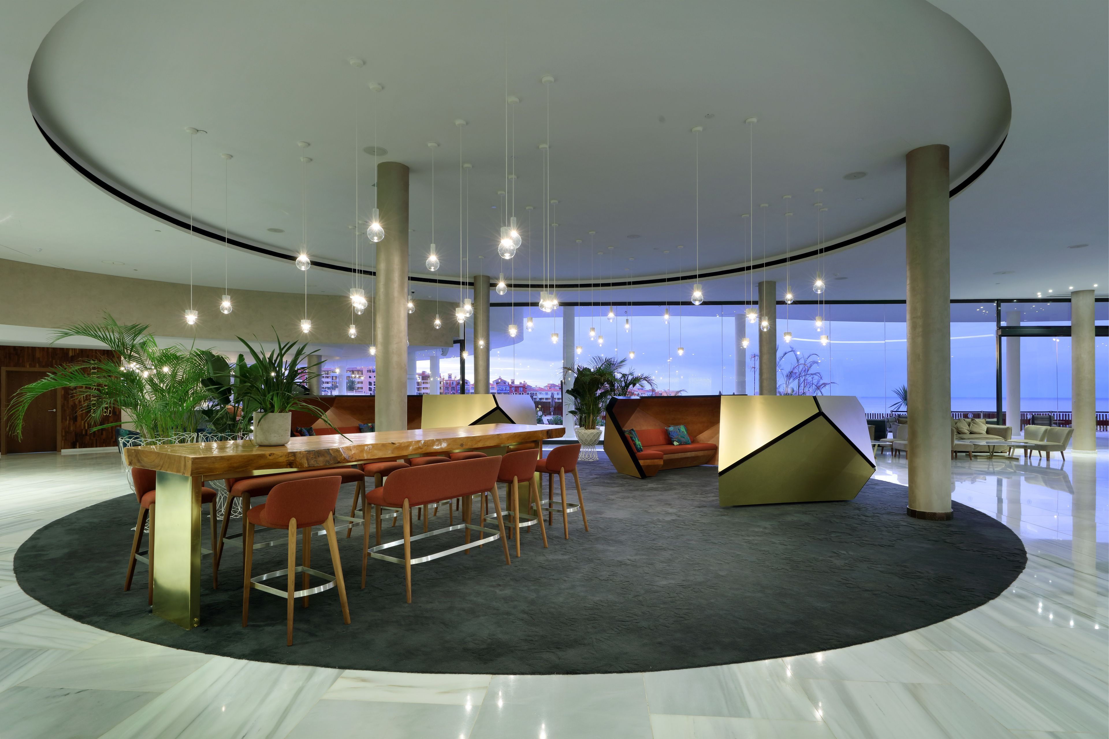 A modern lobby with a circular seating area, a central table, and hanging lights.