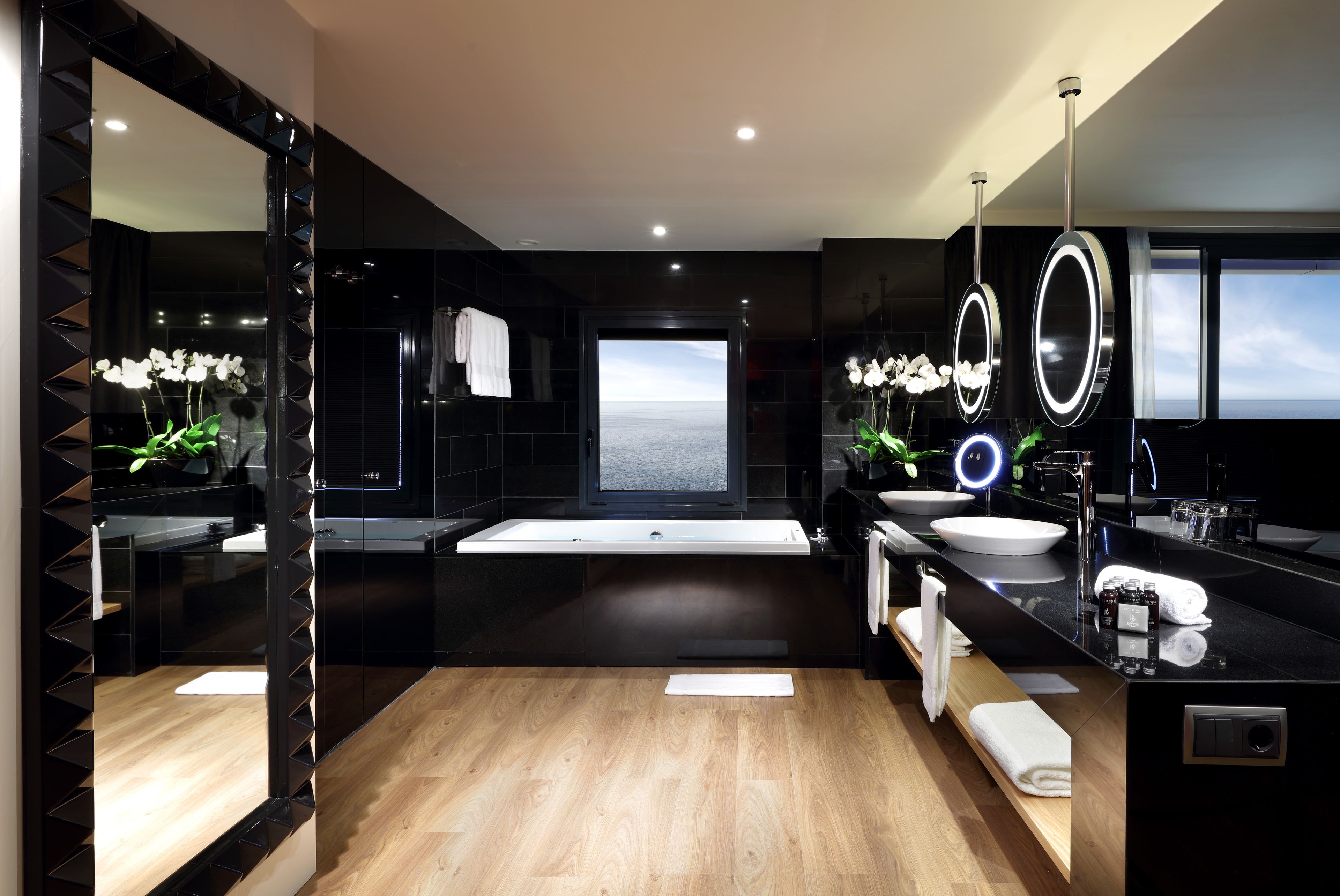 Une salle de bain moderne avec un grand miroir, deux lavabos, une baignoire et une vue sur la mer.