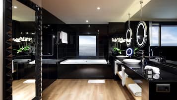 A modern bathroom with a large mirror, two sinks, a bathtub, and a view of the sea.