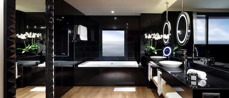 A modern bathroom with a large mirror, two sinks, a bathtub, and a view of the sea.