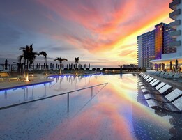 A swimming pool with lounge chairs and palm trees, surrounded by a modern hotel building.