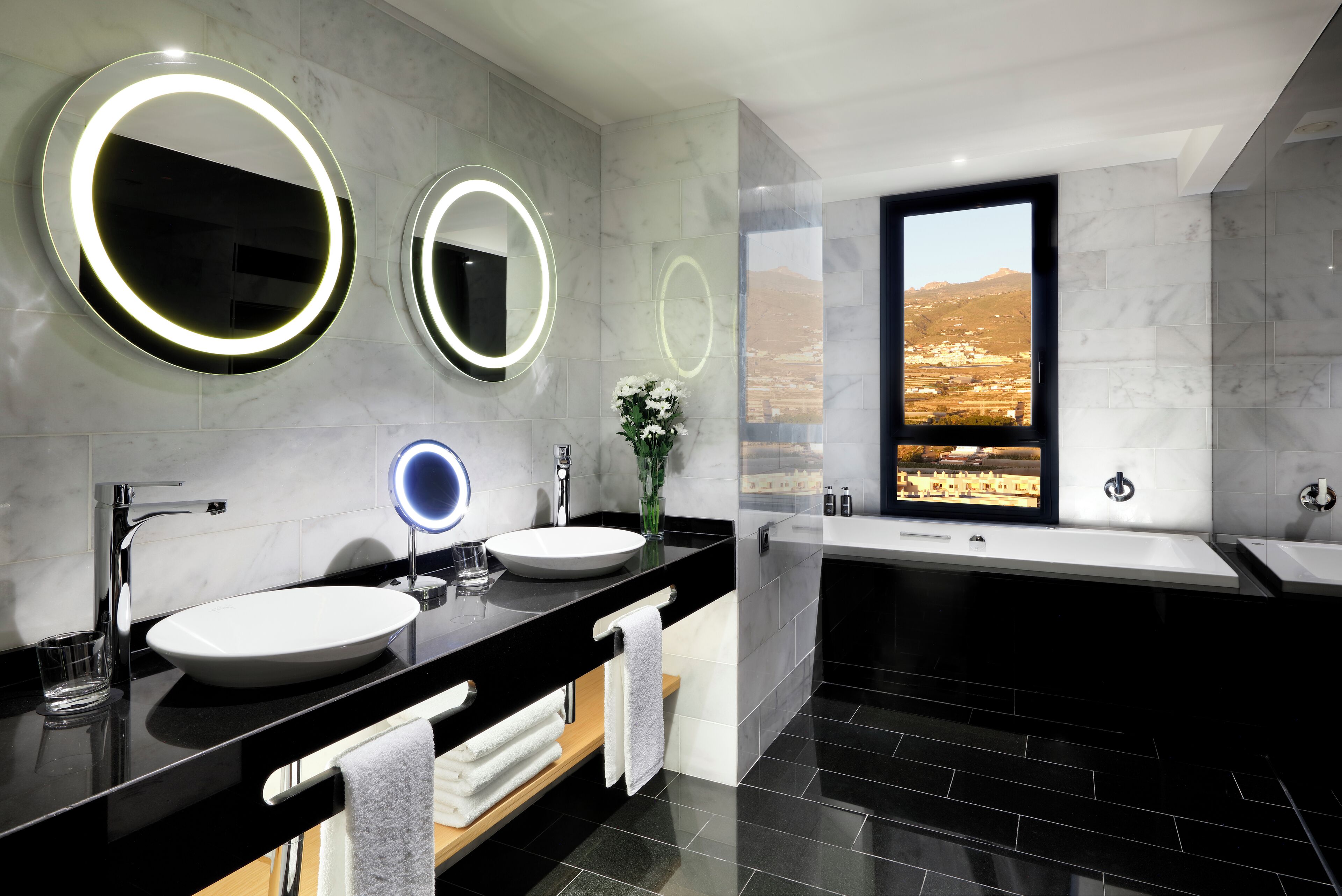 Ein modernes Badezimmer mit zwei runden Spiegeln, einem großen Fenster und einer Badewanne.
