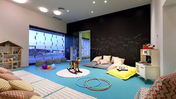 A child-friendly room with a blue carpet, a play area, a bed, and a chalkboard wall.
