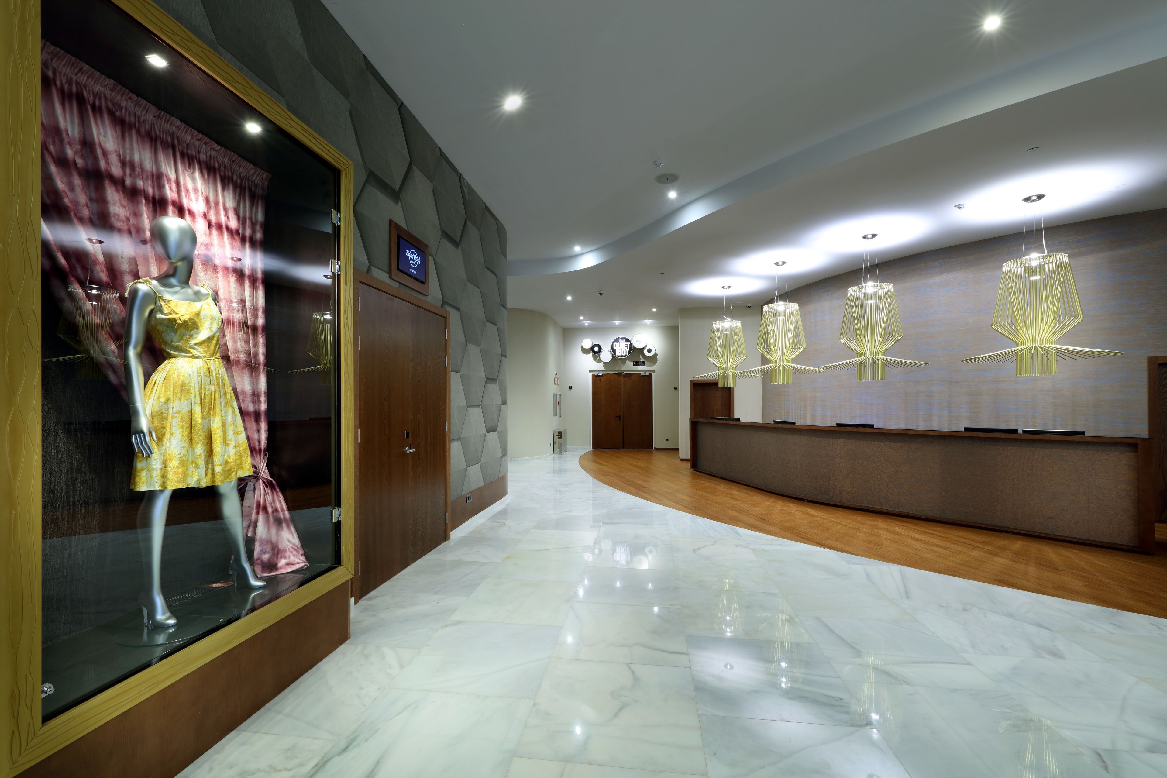 Un vestíbulo de hotel con un maniquí vestido, una recepción y candelabros modernos.