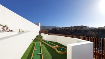 Een dak met een groen kunstgras putting green, een houten golfgat en een witte muur.