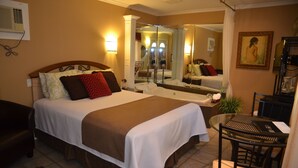 A hotel room with a large bed, a sitting area with a table and chairs, a mirror, and a painting on the wall. - Motel Derfal (Repentigny)