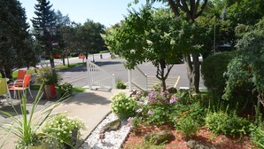 A parking area with a gated entrance, surrounded by landscaped gardens with various plants and flowers. - Motel Derfal (Repentigny)